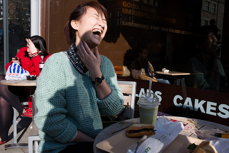 asian woman laughing, sitting at an outside table