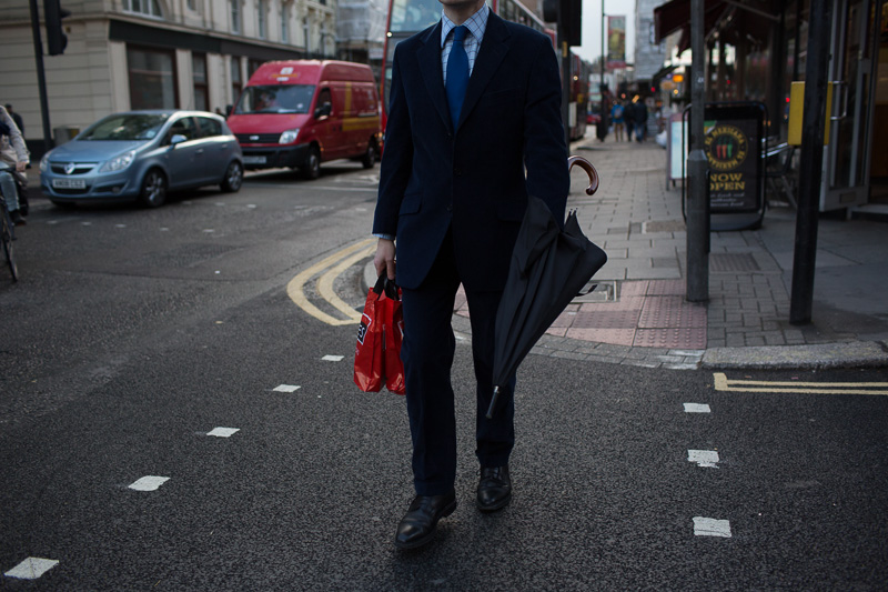 man in a suit walking with his hand inside a folded family size black umbrella, central london, tottenham court road area